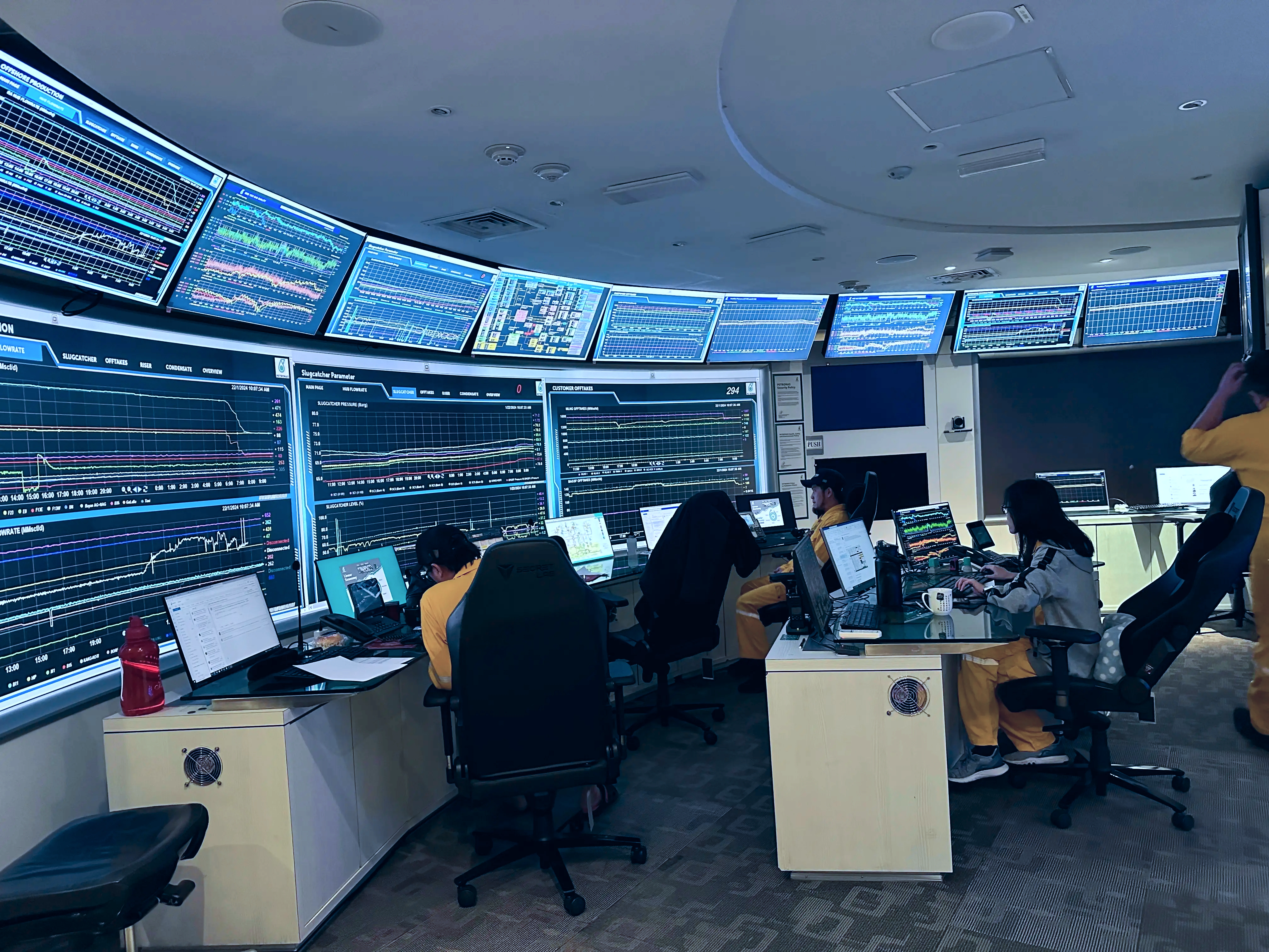 An operations control room with a wall of monitoring screens and operators at their desks.
